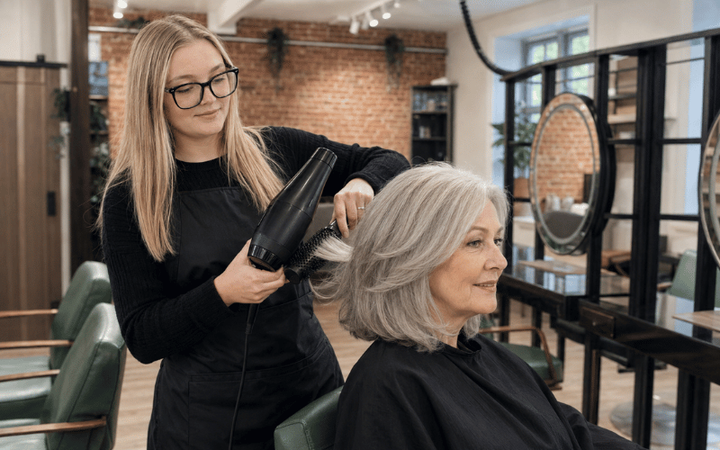 Junior stylist Emily blow-drying an older client’s silver hair at re:new salon in Woodhall Spa