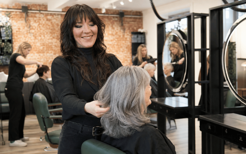 Laura styling an older client’s naturally blended silver-grey hair at re:new salon in Woodhall Spa